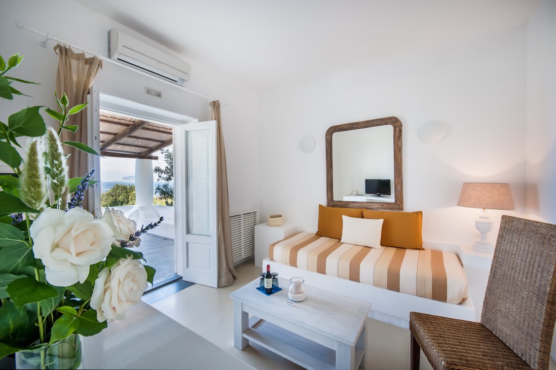 Bright bedroom at Capofaro with striped bedding, sea view through open doors, and fresh white flowers on table.