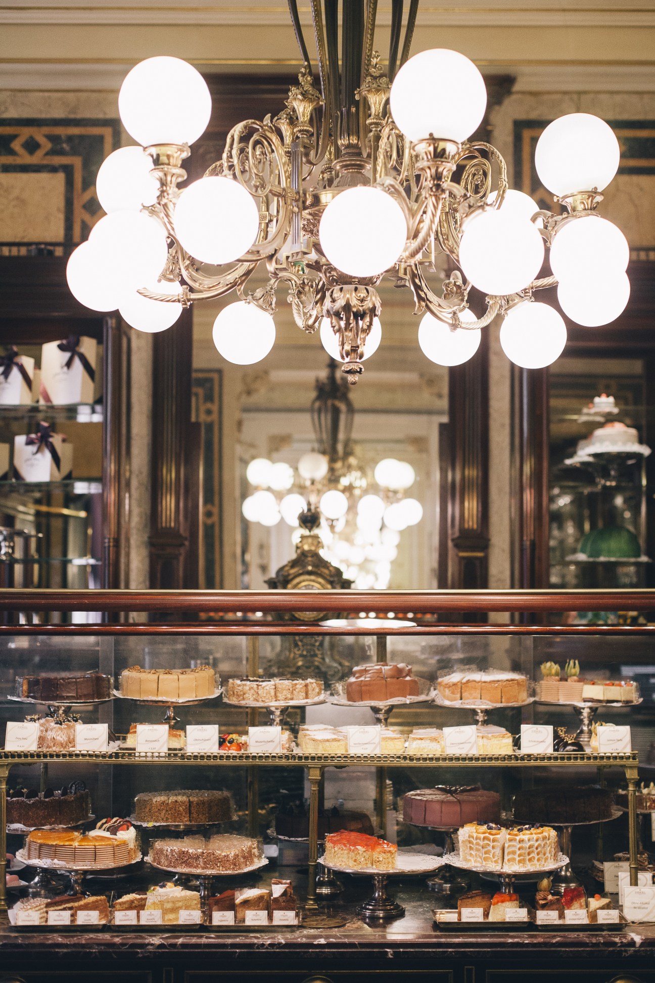 Demel confectionery display with ornate brass chandelier and cakes behind glass counter.