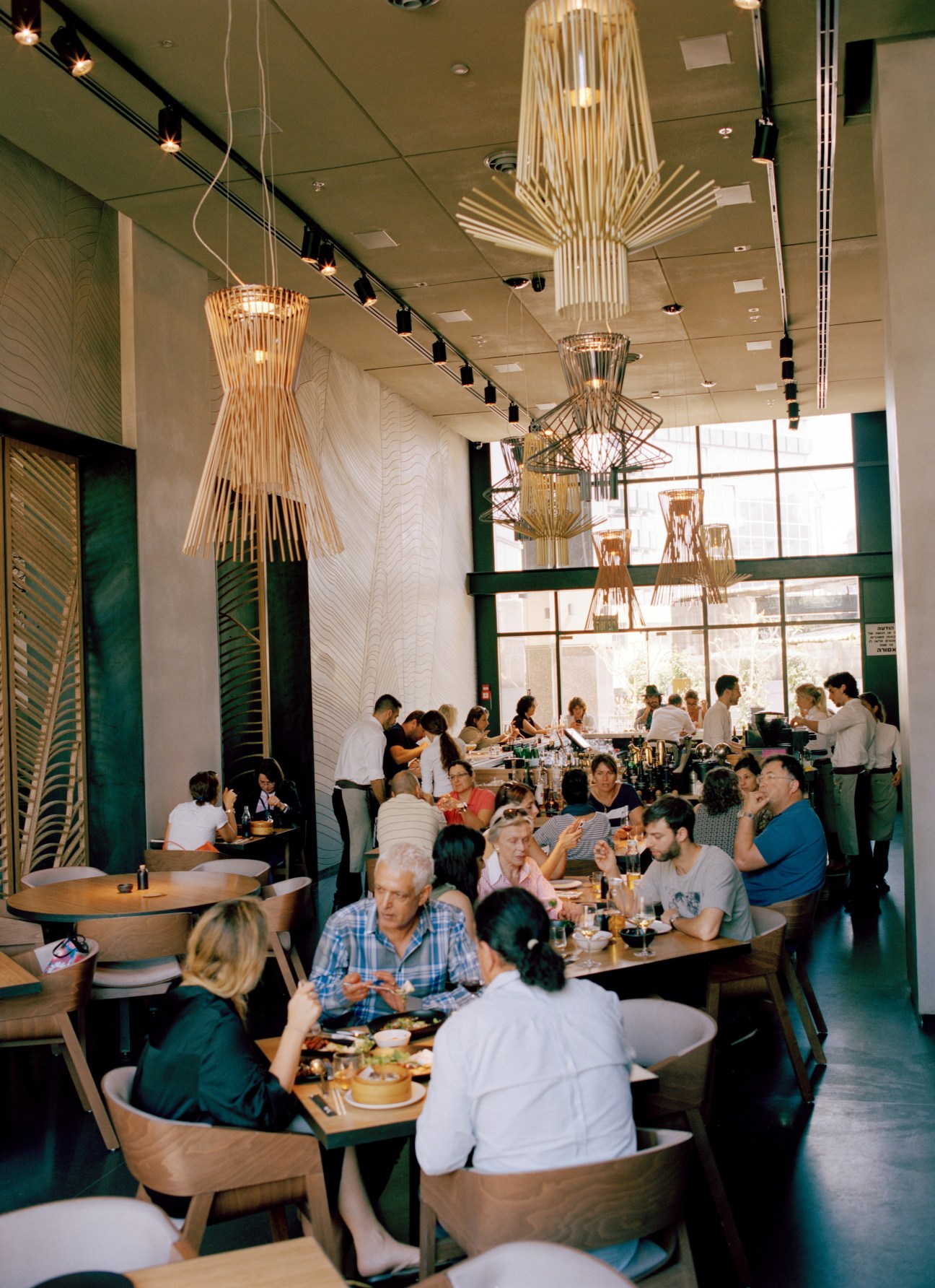 Interior of Taizu Asian restaurant in Tel Aviv with wooden pendant lights and diners at tables.