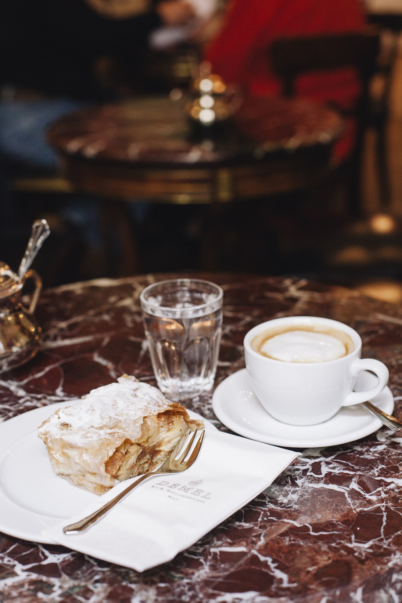 A pastry dusted with powdered sugar and a cappuccino served at a marble table in a Viennese café.