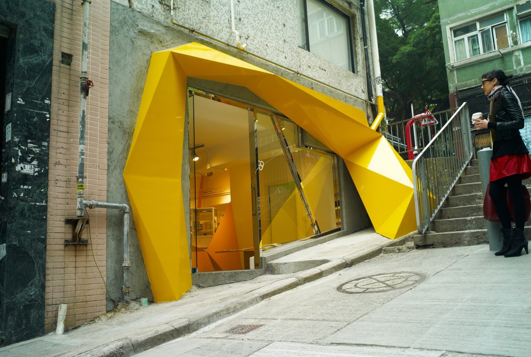 Bright yellow storefront with geometric angular design on a narrow street in Hong Kong's Sheung Wan district.