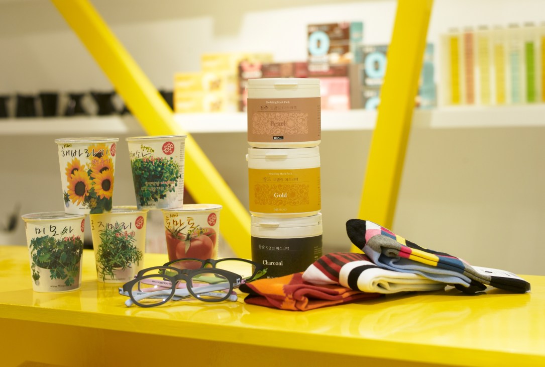 Korean beauty products and magazines displayed on a bright yellow surface with eyeglasses.