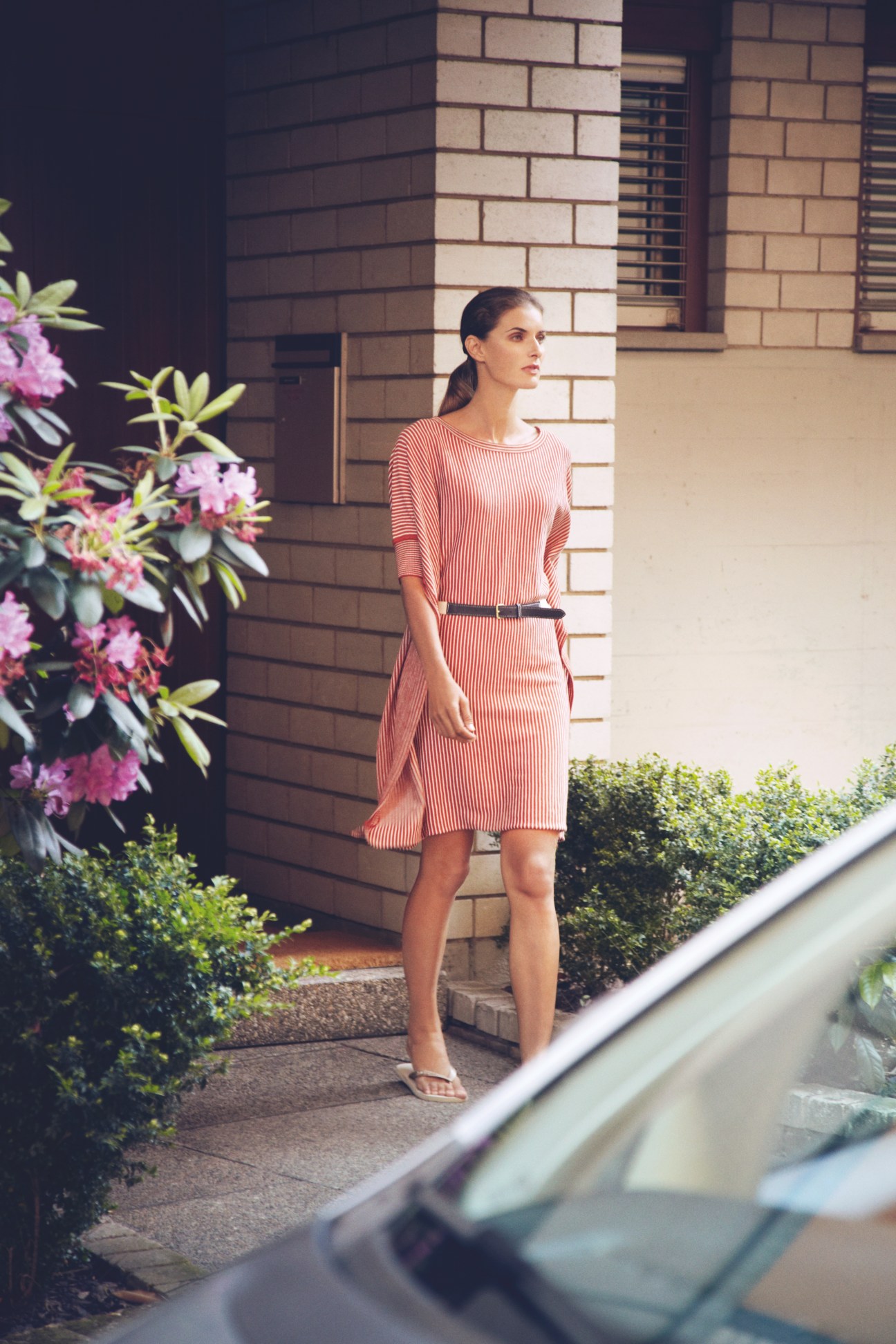 Woman wearing a coral striped dress by Iliann Loeb and Havaianas flip flops standing in front of a modernist brick building.