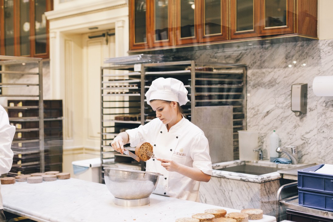 A pastry chef in white chef's coat and hat preparing baked goods in Demel's kitchen.