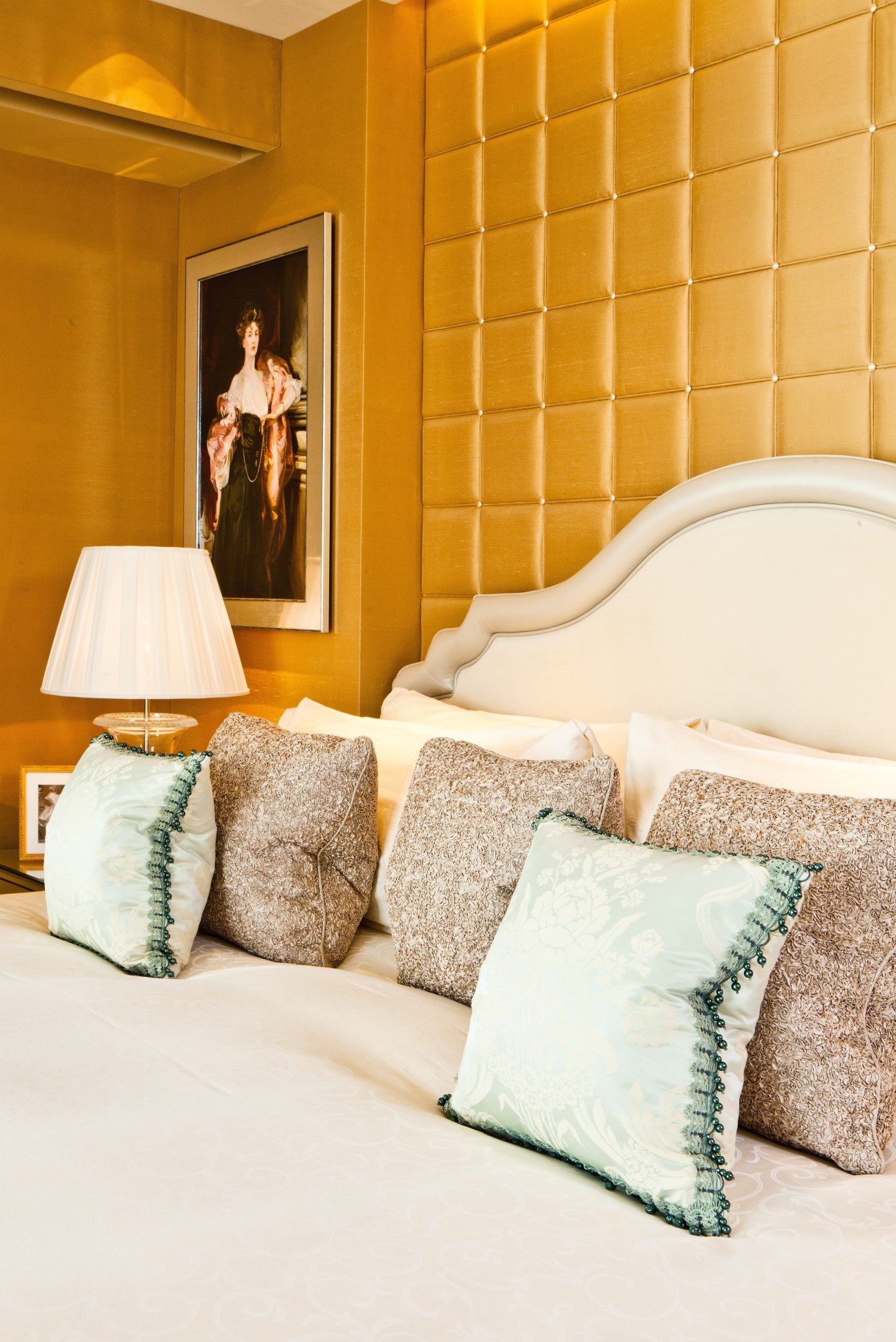 Luxury hotel bedroom with gold quilted wall paneling, white curved headboard, and decorative pillows.