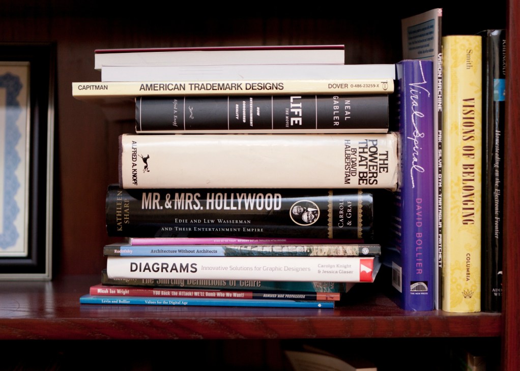 Stack of reference books on a wooden shelf including titles on American trademark designs, life, architecture, and diagrams.