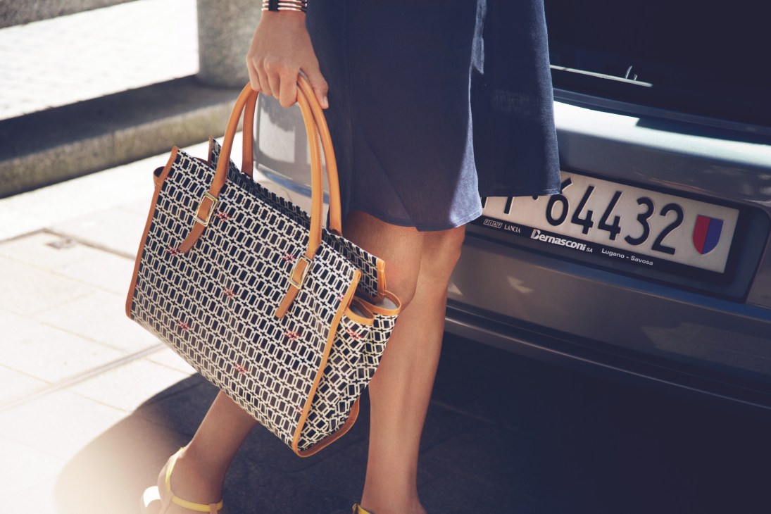 Woman holding a patterned Roger Vivier bag next to a Lancia car in Lugano.