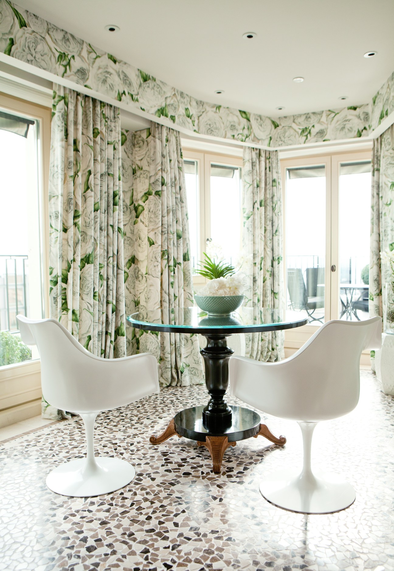 Elegant curved room with floral wallpaper, white modern chairs, and glass doors opening to terraces.