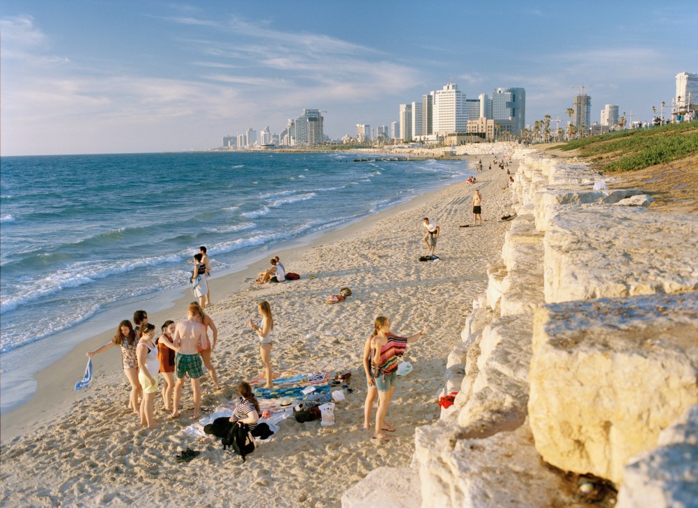 Tel Aviv's sandy beach with swimmers and sunbathers, high-rise buildings and palm trees lining the shore
