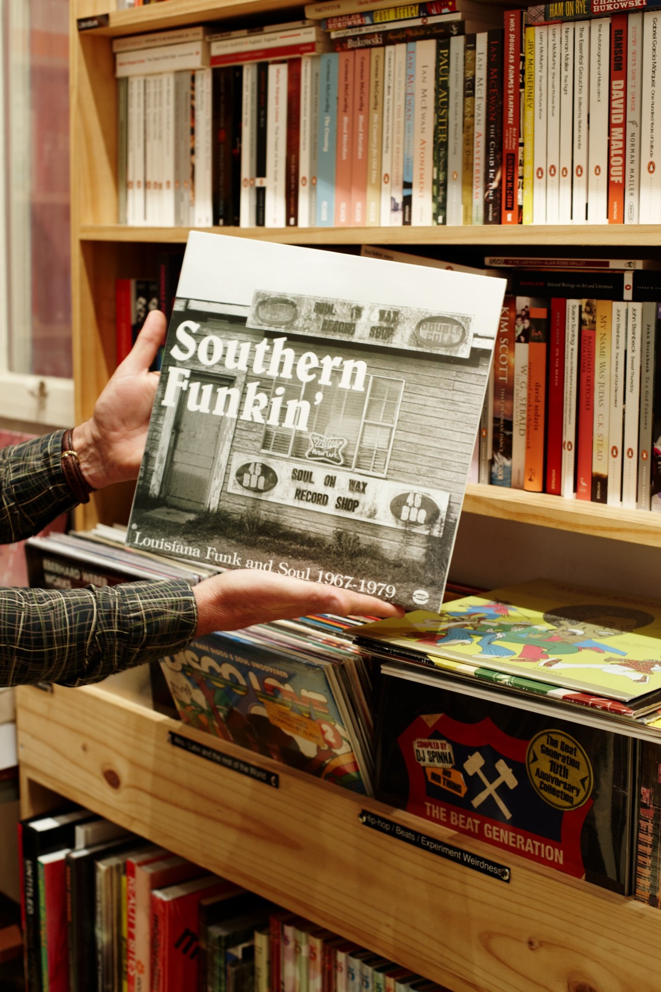 Person holding a Southern Funk and Soul vinyl record in TITLE music store with shelves of CDs and books visible behind.