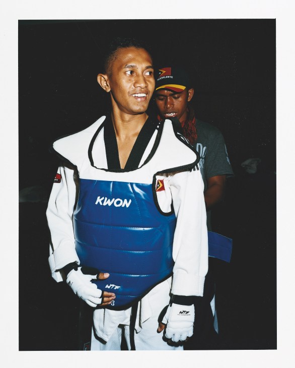 Timor Leste taekwondo athlete in white protective gear and blue chest protector with KWON branding.