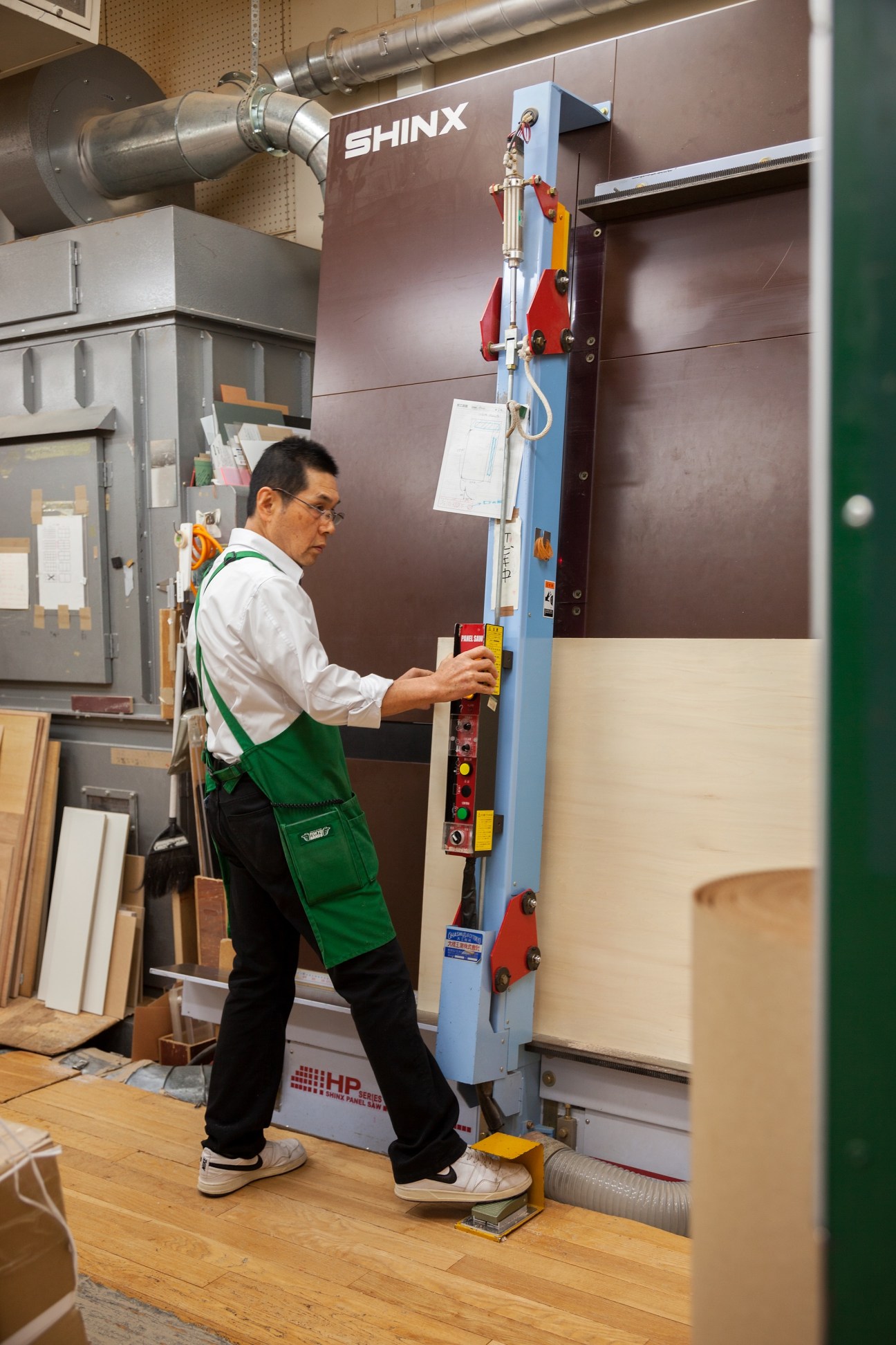 A Tokyu Hands staff member in green apron operates a SHINX woodworking machine in the store's wood workshop.