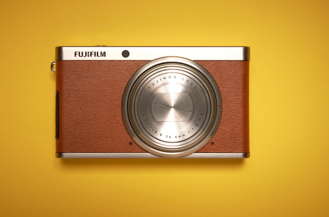 Fujifilm XF1 compact camera with brown leather body and silver top plate on yellow background.