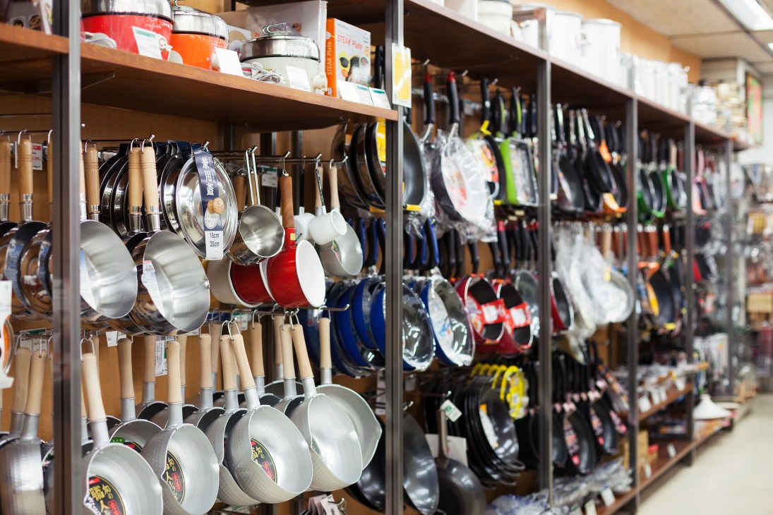 Kitchen pans and cookware with wooden handles displayed on wall-mounted shelves.