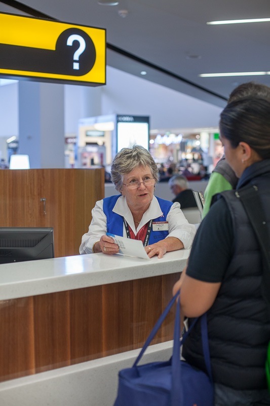 Elderly female staff member assisting passenger at Auckland Airport information desk