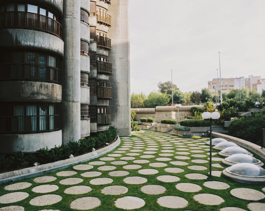 Torres Blancas rooftop terrace with circular concrete stepping stones set into green grass, cylindrical building with rounded balconies, and Madrid cityscape beyond.