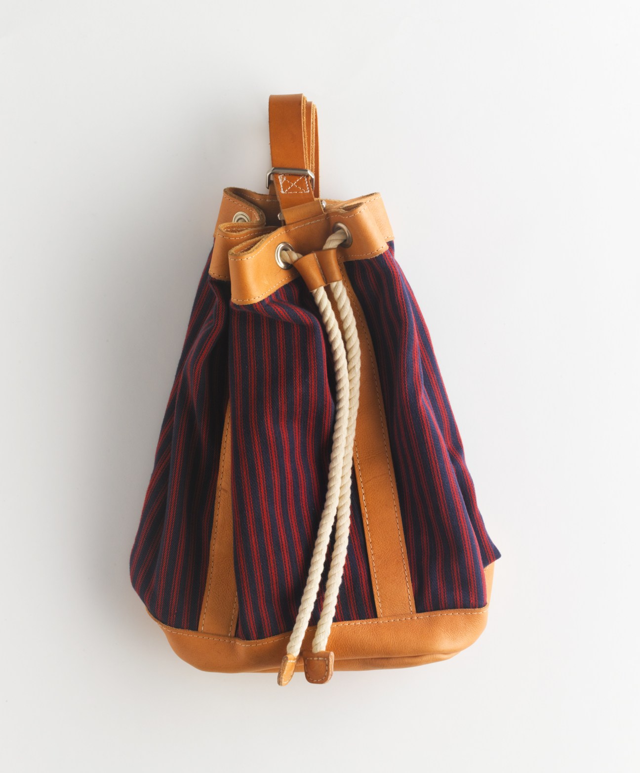 Tan leather bucket bag with navy and red striped fabric and cream rope drawstring by Billykirk.