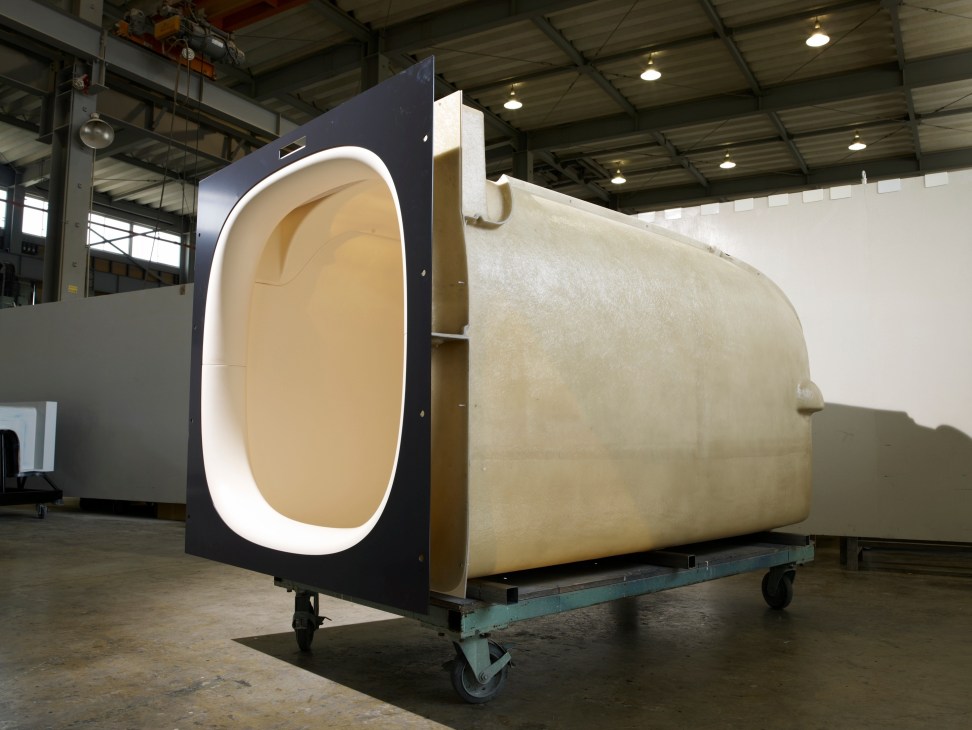 A modern capsule hotel sleeping pod with black exterior and illuminated white oval entrance in an industrial setting.