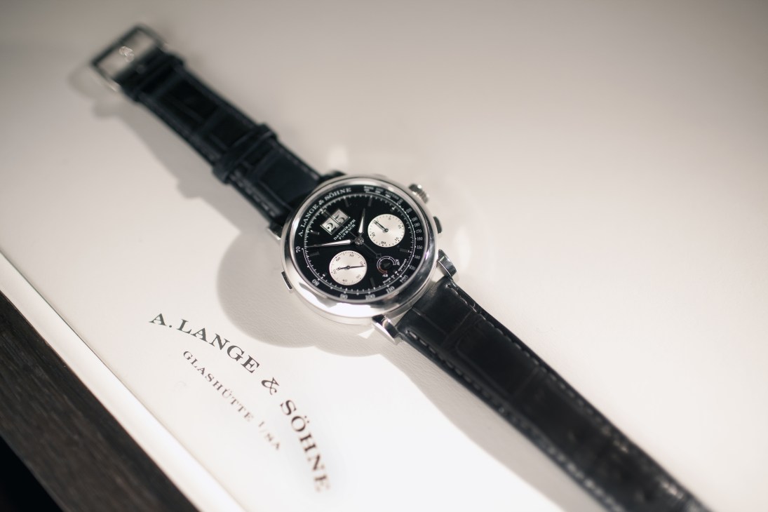 A Lange & Söhne Datograph Up/Down chronograph watch with black dial and leather strap displayed on branded packaging.