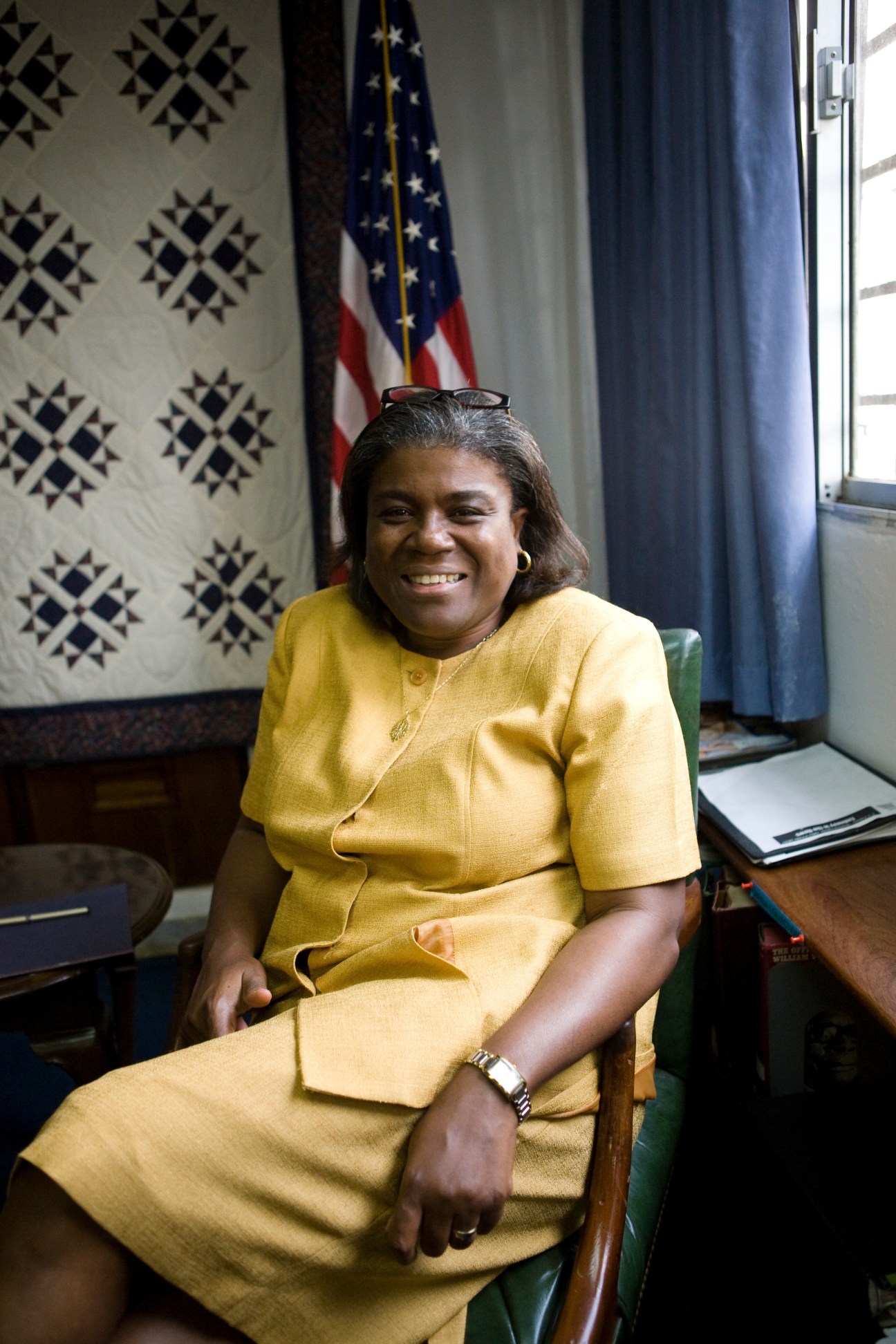 US ambassador Linda Thomas-Greenfield sitting in a yellow dress in front of an American flag