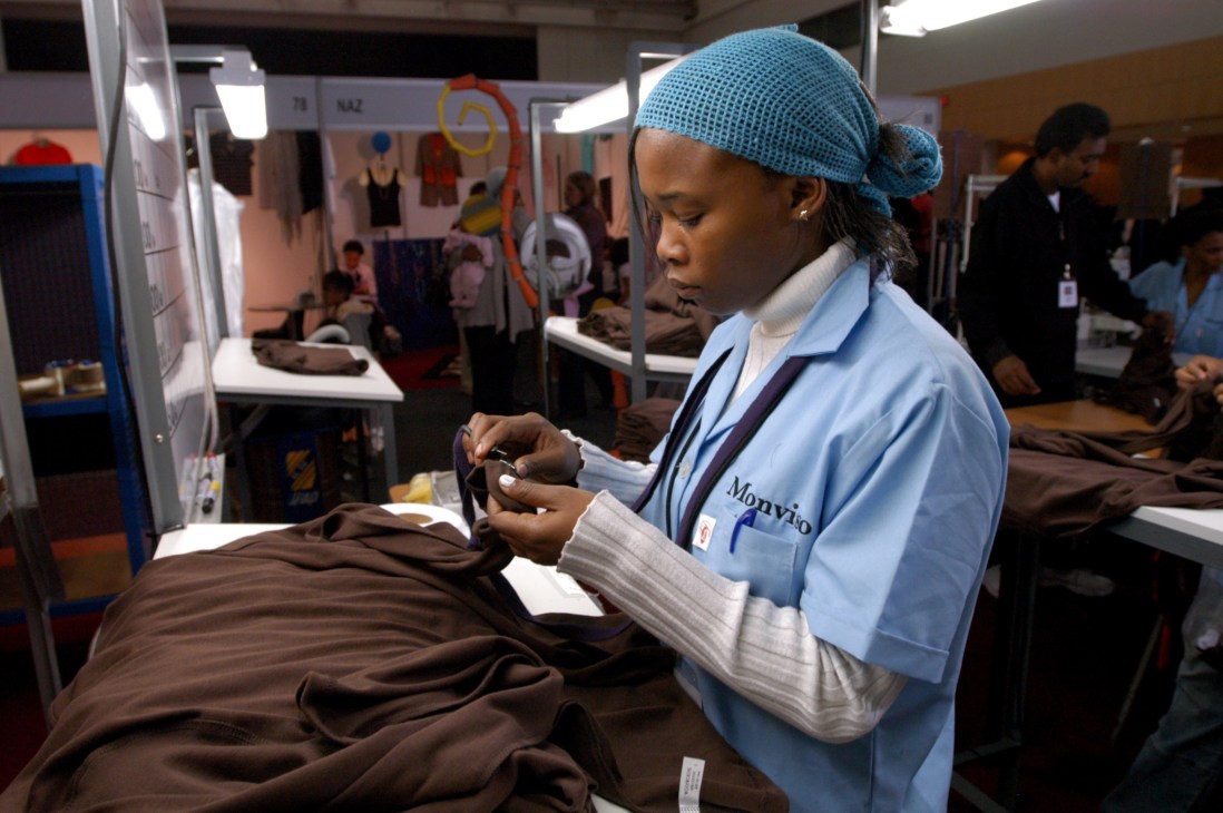 Woman in blue Mouyido work uniform inspecting brown fabric at clothing manufacturing facility.