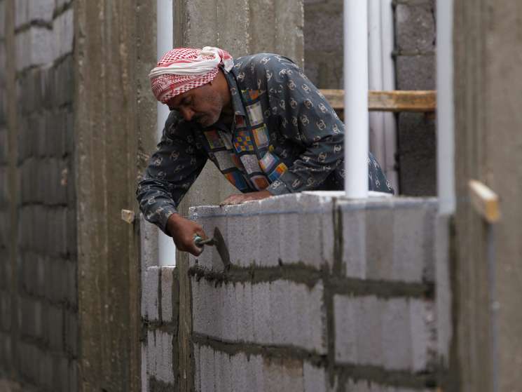 Worker in traditional Middle Eastern dress laying concrete blocks on a construction site.