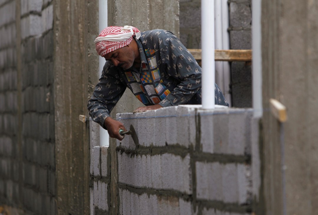 Worker in traditional Middle Eastern dress laying concrete blocks on a construction site.