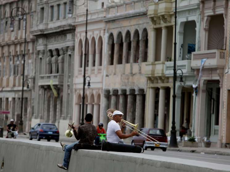 Musicians playing brass instruments on Havana's Malecón seafront promenade with colonial buildings in the background.