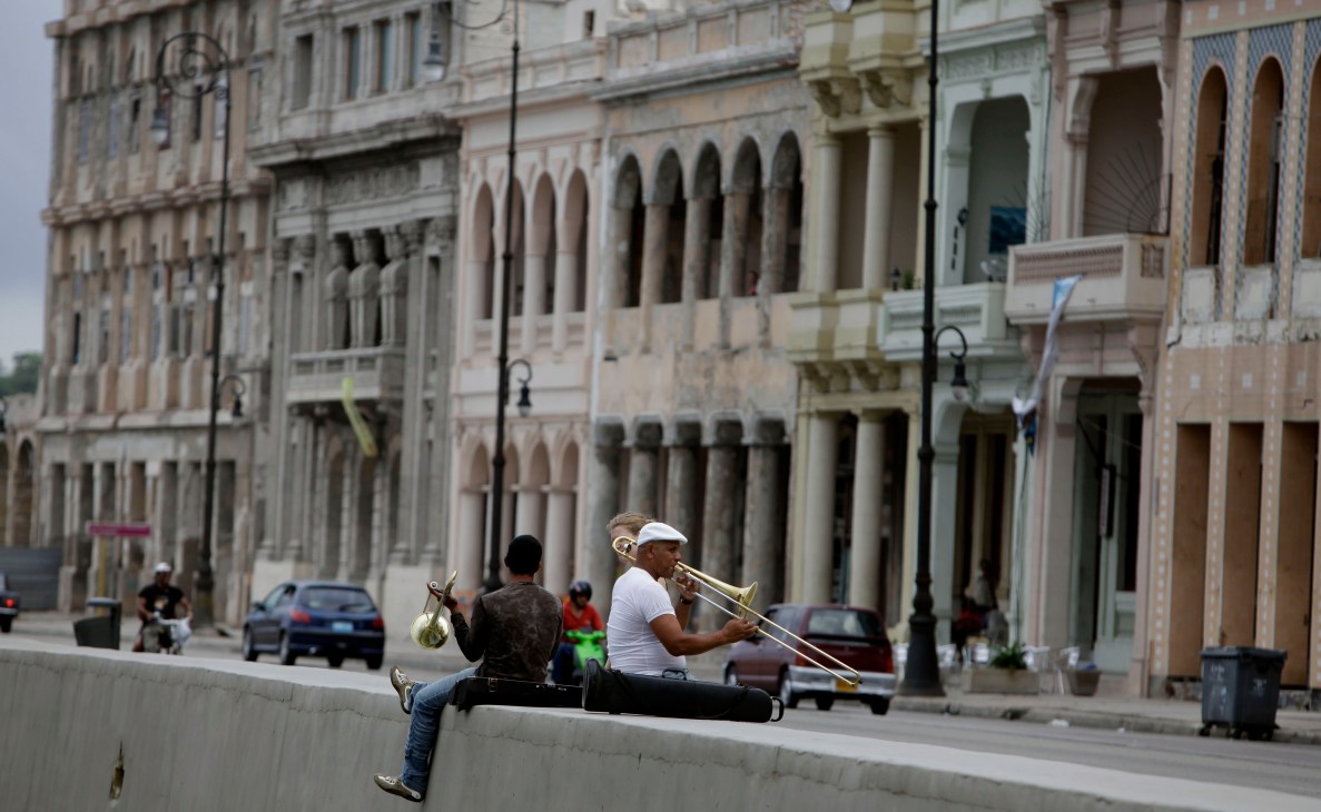 Musicians playing brass instruments on Havana's Malecón seafront promenade with colonial buildings in the background.