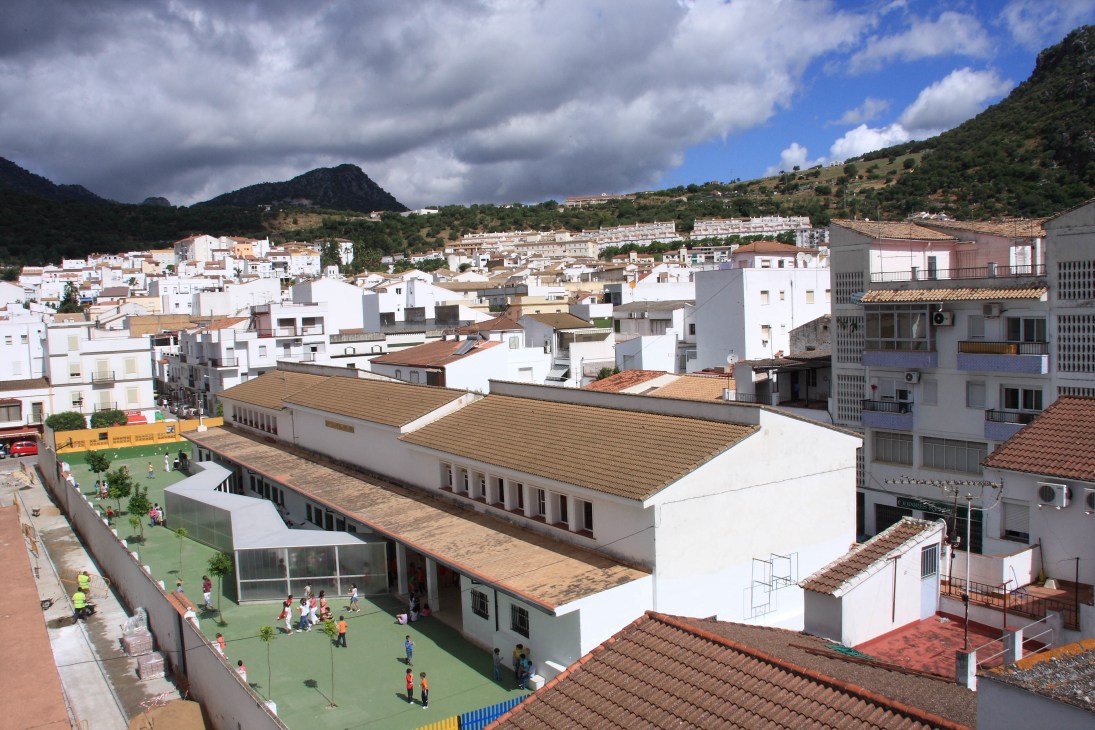 Aerial view of Victor de la Serna y Espina school in Ubrique, Spain, showing modern white buildings with wooden roofs amid a hillside town.