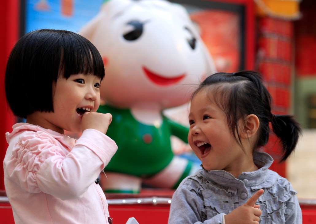 Two young children laugh in front of a large smiling cartoon character mascot.