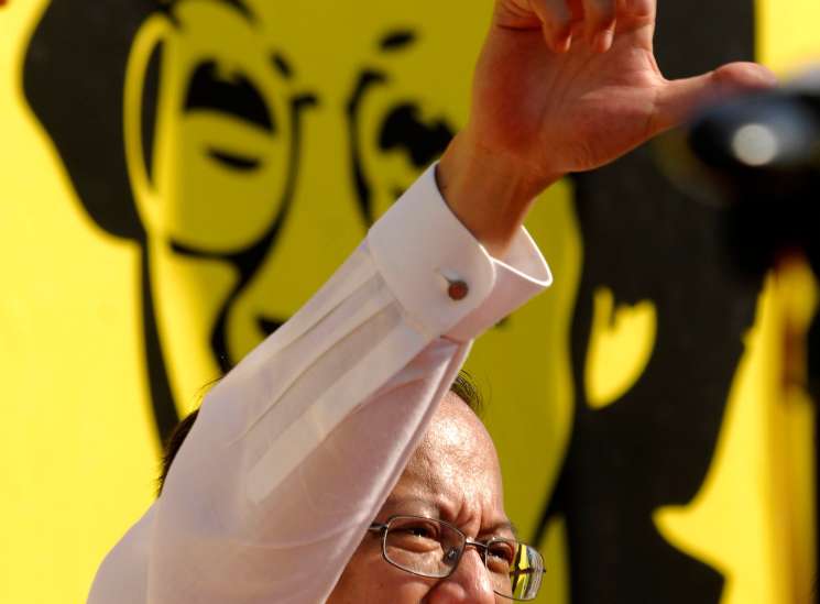 Man in glasses and white shirt making a peace sign with yellow propaganda posters in background.