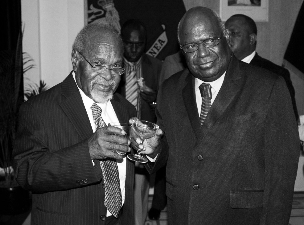Two men in suits holding drinks at an official event in black and white photograph.