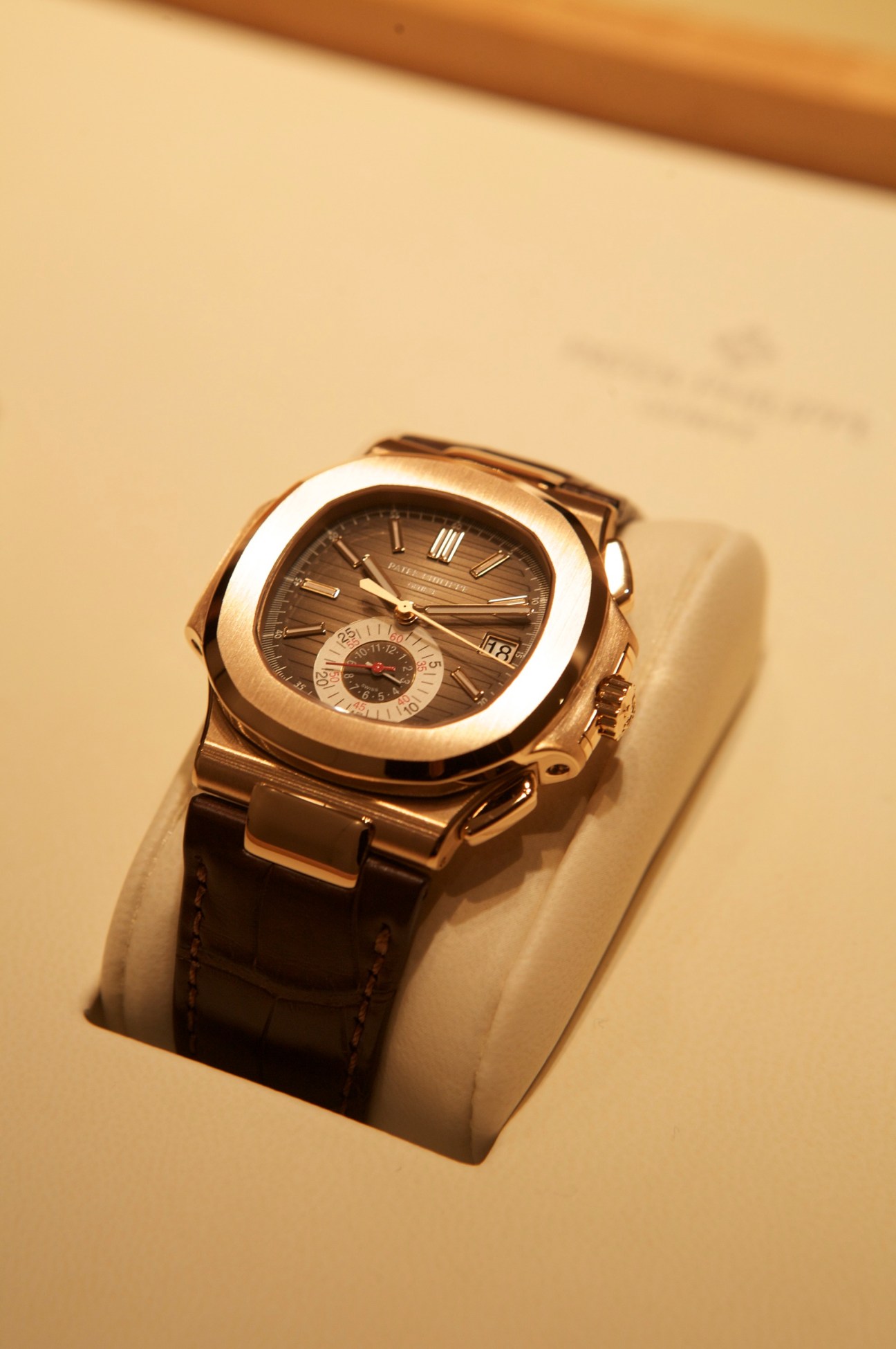Patek Philippe Nautilus watch in rose gold with black leather strap displayed on cream-colored stand.
