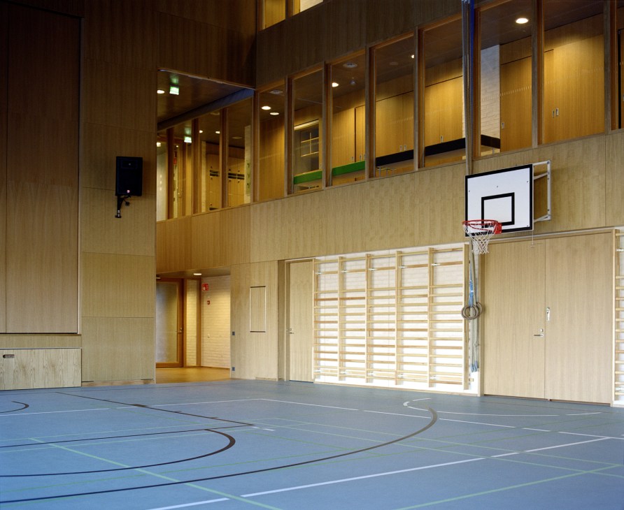 Interior of Kirkkojärvi School's beech gymnasium with basketball hoop and wooden cladding.