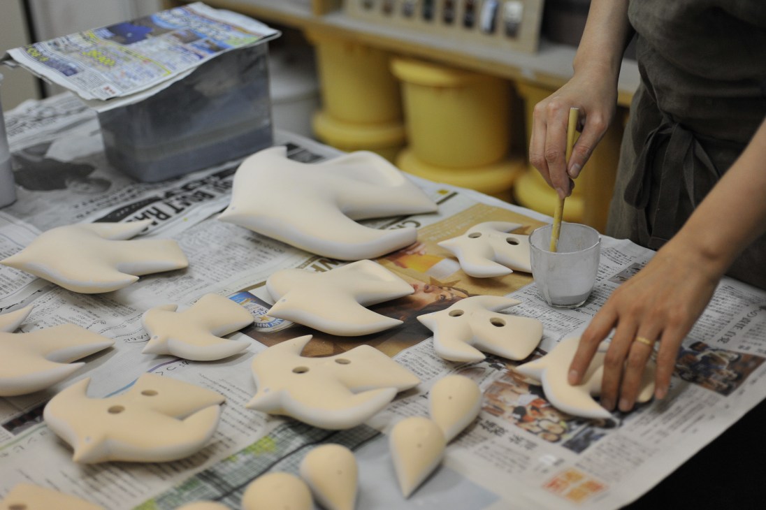 Potter Rie Ito works on ceramic bird sculptures at her studio workbench covered with newspaper.