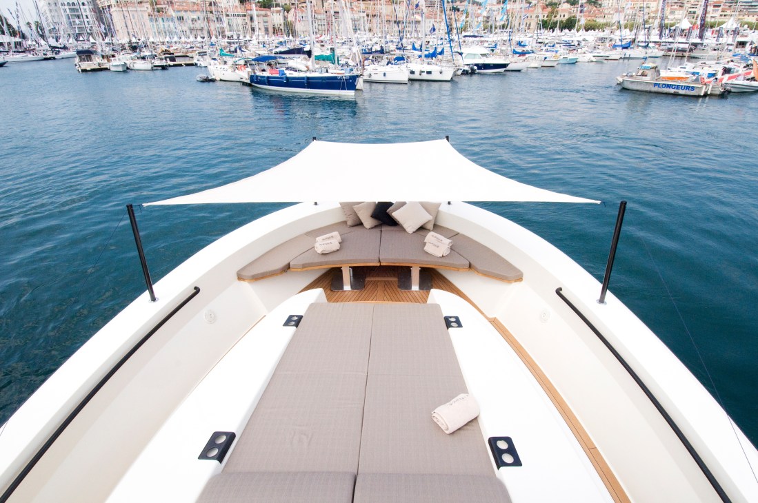 Bow of a Bluegame 60' motor yacht with teak seating, white canopy and moored boats in Cannes harbour behind.