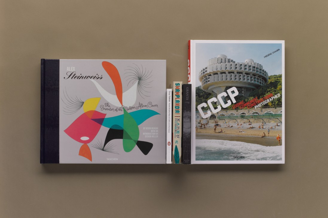 A collection of design and photography books displayed on a shelf against a beige wall.
