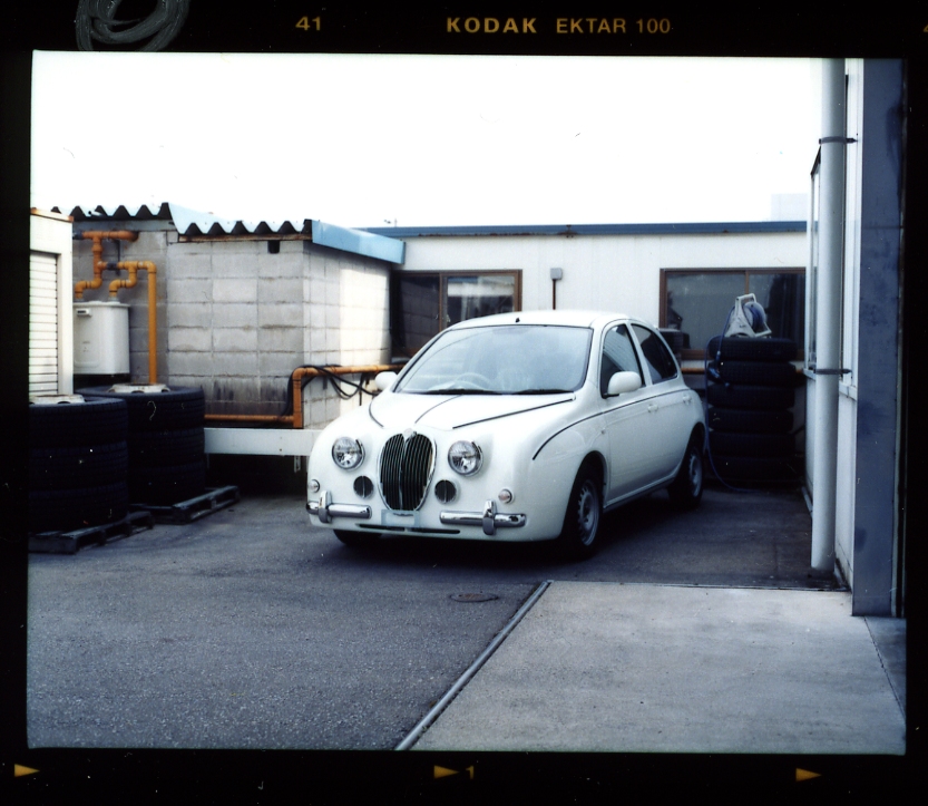 White Mitsuoka Viewt, a retro-styled car inspired by the Jaguar Mk1, parked in a factory courtyard.