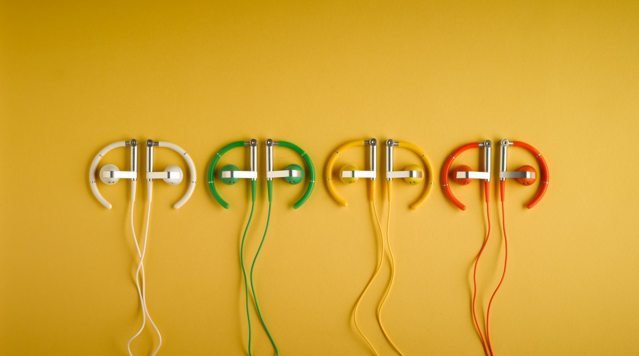Four Bang & Olufsen headphones in white, green, yellow, and red against a yellow background.