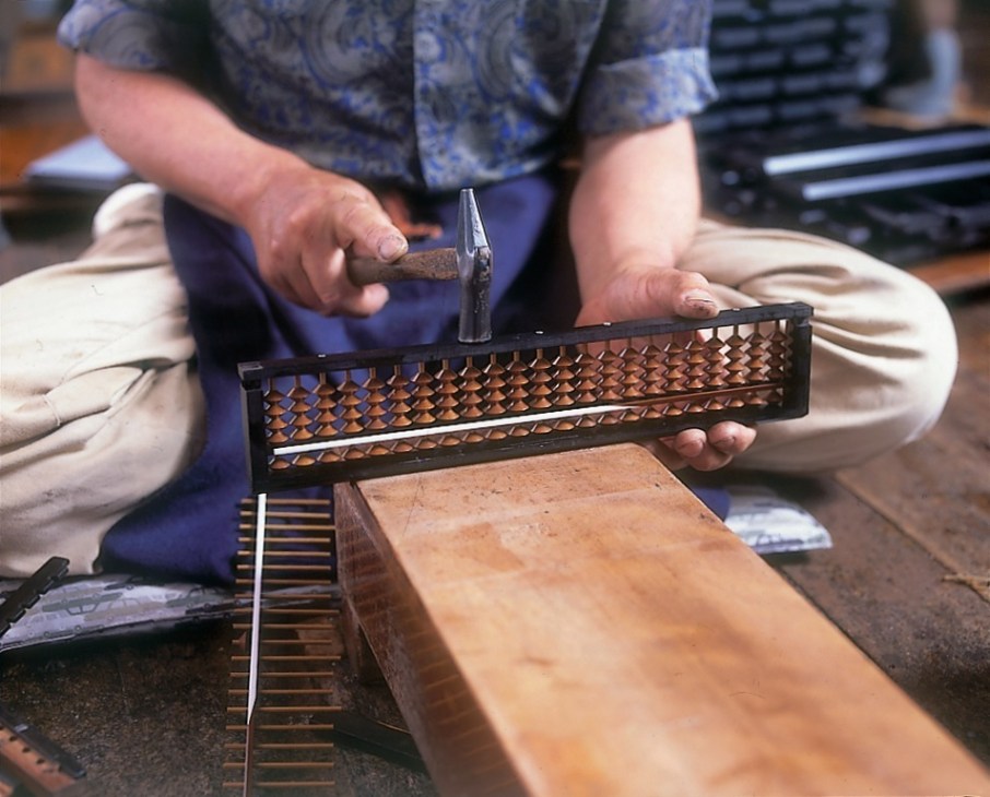 Hands assembling a wooden soroban abacus with metal beads and frame.