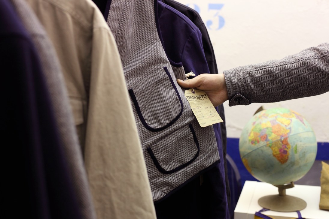 A person examines a grey textured jacket with a Taylor Supply label at a trade show display.