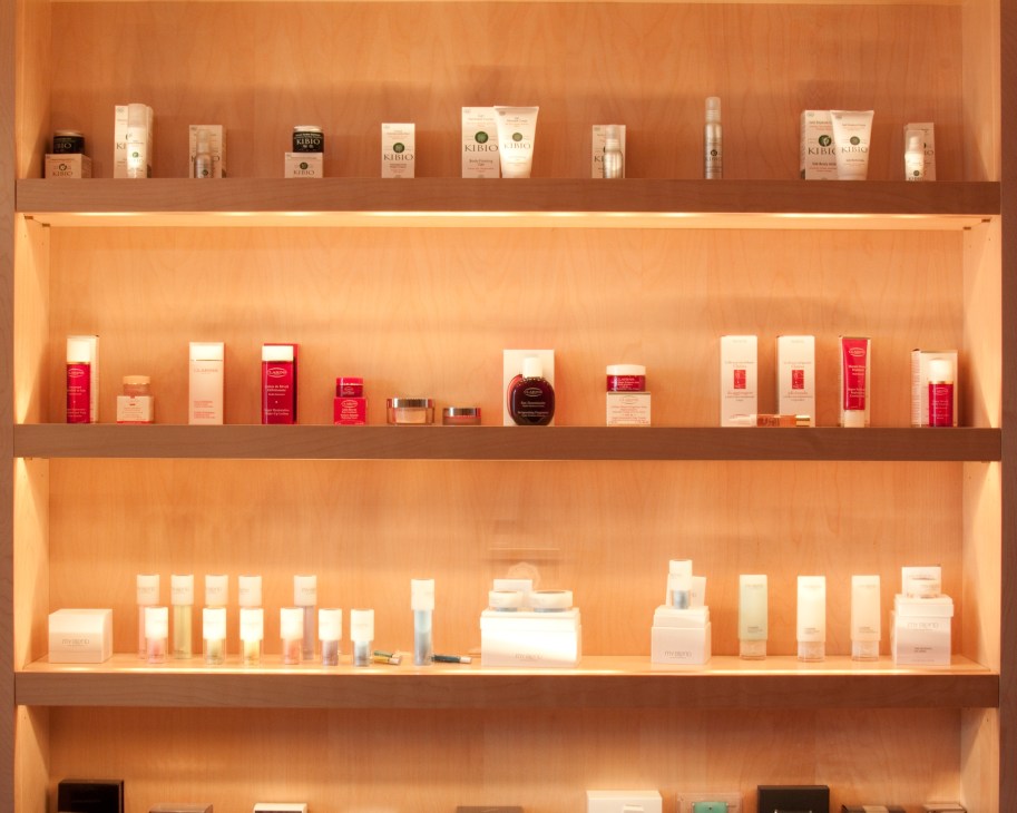 Clarins beauty products displayed on illuminated shelves showing the brand's distinctive packaging in cream, white, and red bottles and jars.