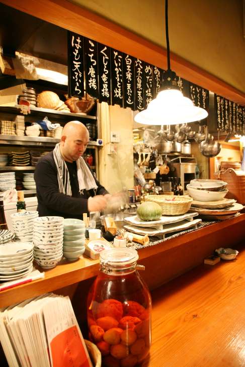 Owner-chef Munehiro Ikeda working behind a wooden sushi counter at Ikedaya restaurant in Tokyo.
