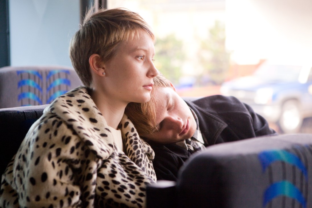 Young woman in leopard print coat gazes thoughtfully out a window from public transport.