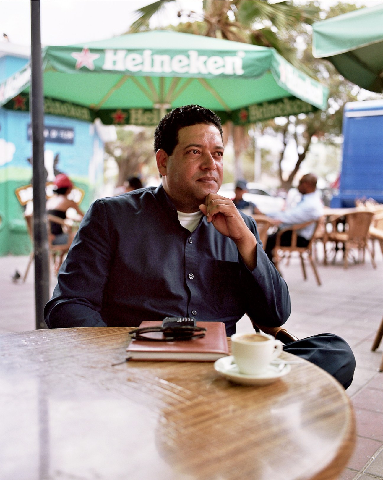 Alex Rosaria, former Antilles state secretary of finance, sitting at an outdoor café table under a Heineken umbrella.