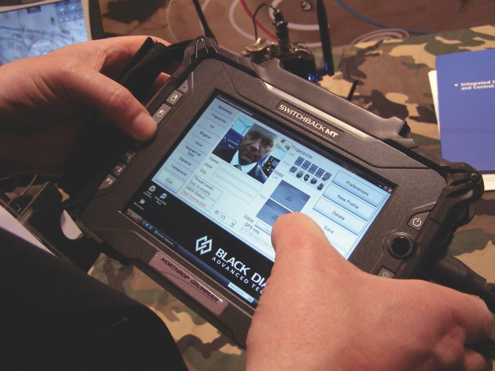 Hands holding a BioTRAC device displaying facial recognition and biometric data on screen.