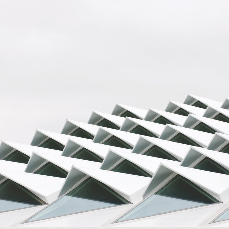 Geometric white roof detail with triangular glass panels and dark interior shadows against a light sky.