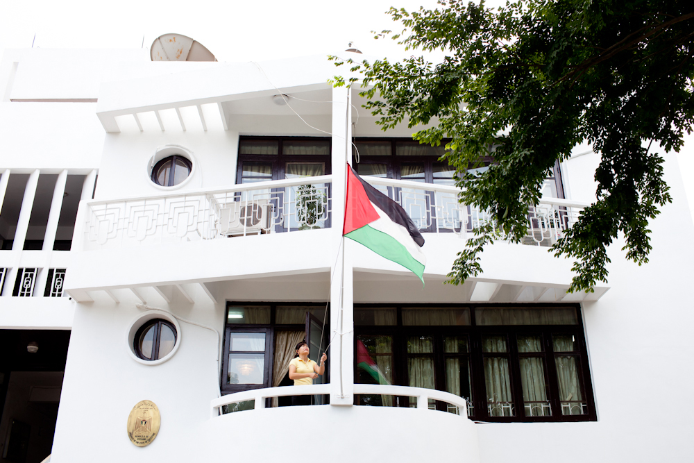 Palestinian flag flying outside a white modern building with a person visible in a window.