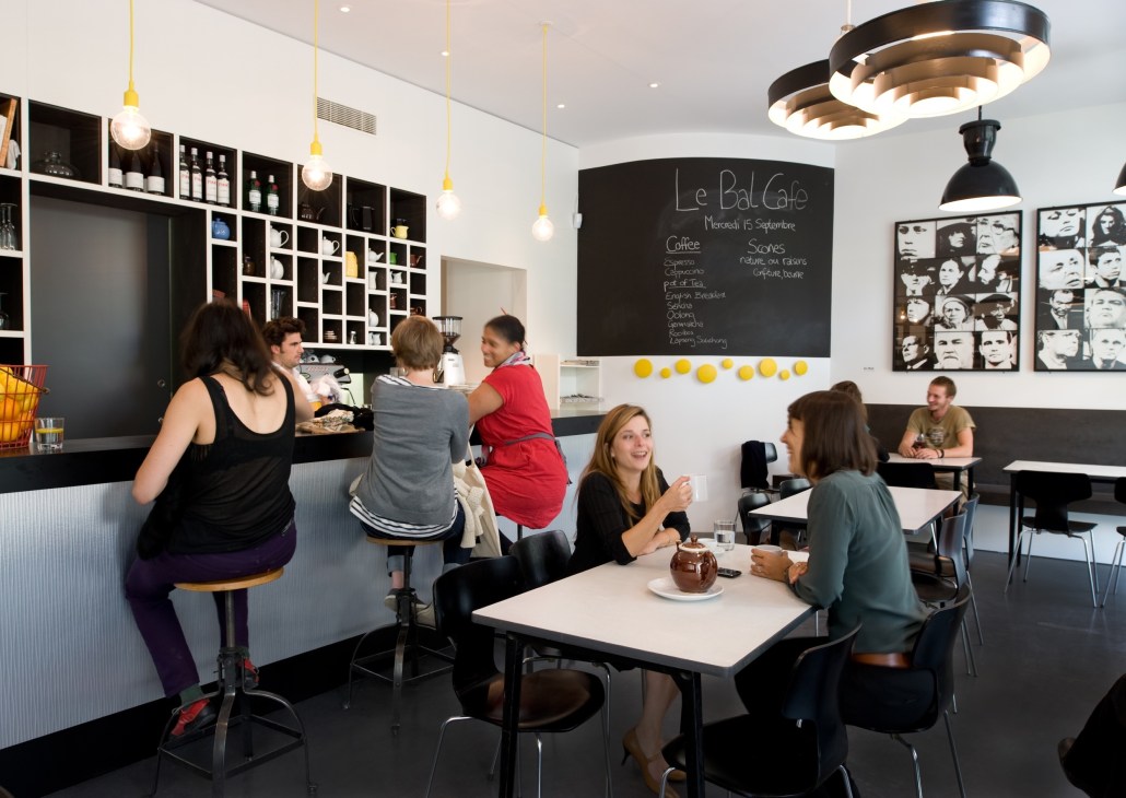 Interior of Le Bal Café in Paris with customers at tables and counter, featuring modern black and white design with pendant lighting.
